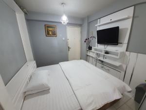 um quarto com uma cama branca e uma televisão de ecrã plano em Bassura City Apartment by Sang Living em Jacarta
