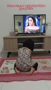 a child sitting on a rug watching a television at Cikgu Huda Homestay Bajet in Seri Manjung