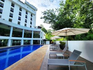 una piscina con sillas y una sombrilla junto a un edificio en The Palace Hotel Kota Kinabalu en Kota Kinabalu