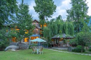 a house with a table and chairs and an umbrella at StayVista at The Waterwillow with Valley View in Manāli