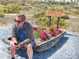 a man sitting on a bench next to a flower garden at Bokkomblommetjie in Lambertʼs Bay