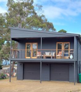 a gray house with a balcony and tables and chairs at The Beach Box at Big Roaring Beach Tasmania in Surveyors Bay