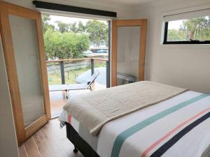 a bedroom with a bed and a balcony with a window at The Beach Box at Big Roaring Beach Tasmania in Surveyors Bay