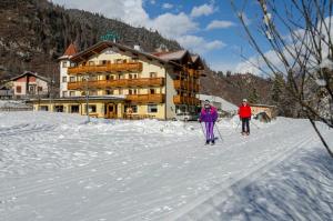 Due persone sugli sci nella neve di fronte a una casetta di Hotel Valsorda a Moena