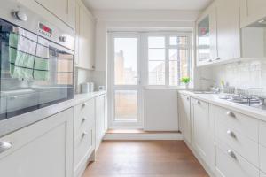 a white kitchen with white cabinets and a window at Stylish and Central 1 Bedroom Flat in Maida Vale in London