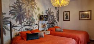 1 dormitorio con 2 camas con sábanas de color naranja y un mural de palmeras en Casa Rural El Canto Del Agua, en Malpartida de Plasencia