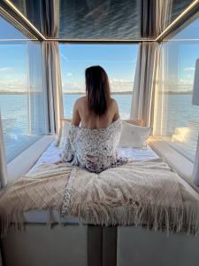 a woman sitting on a bed in front of a window at HT Houseboats - domki na wodzie - sauna, lake view in Mielno