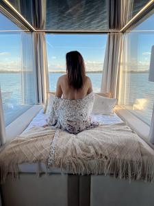 a woman sitting on a bed in front of a window at Domki na wodzie - HT Houseboats - with sauna, jacuzzi massage chair in Mielno