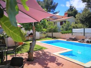 a swimming pool with an umbrella next to a house at Apartments Bilic with garden & swimming pool - 50m from the beach in Pješčana Uvala 
