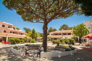 eine Person, die auf einer Bank unter einem Baum sitzt in der Unterkunft Falesia Beach A in Albufeira