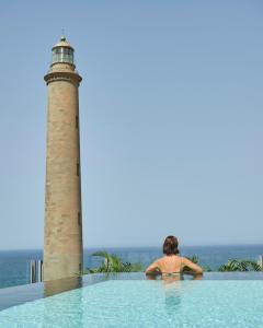 a woman in a swimming pool next to a lighthouse at Hotel Faro, a Lopesan Collection Hotel - Adults Only in Maspalomas