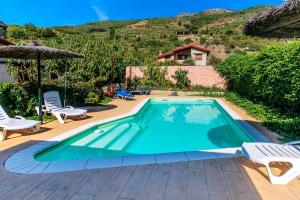 a swimming pool with two chairs and an umbrella at casa rural La picotina in Navaconcejo