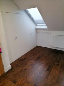 an attic room with a skylight and white walls and wood floors at Grand 4 Bed 3 Bath House Chadwell Heath, Romford, London in Goodmayes