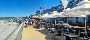 a beach with tables and chairs and white umbrellas at Les Fregates in Veulettes-sur-Mer