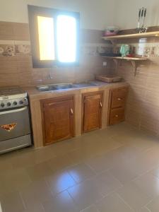 eine Küche mit Holzschränken, einem Waschbecken und einem Fenster in der Unterkunft Auberge Keur Ely in Ouoran