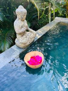 una ciotola di fiori rosa seduta accanto a una statua in piscina di Ô Palm : dans un petit écrin de verdure a Saint-Joseph