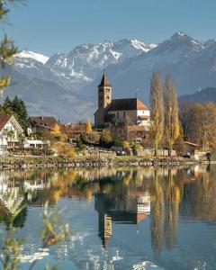 a church sitting next to a lake with snow covered mountains at Apartments am See in Brienz