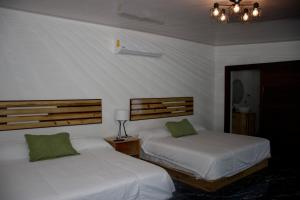 two beds in a bedroom with white sheets and green pillows at Hotel Samoa del Sur in Golfito