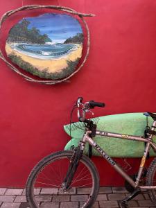 uma bicicleta estacionada ao lado de uma parede vermelha com um quadro em Aldeia de Camburi em Camburi
