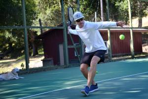 un hombre balanceando una raqueta de tenis en una pelota de tenis en The Camp at Carmel Valley, en Carmel Valley