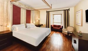 a hotel room with a large white bed and a chair at NH Collection Palacio de Burgos in Burgos