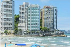 a beach with umbrellas and people in the water and buildings at Pé na Areia a Poucos Metros -Apartamento Guarujá Pitangueiras in Guarujá