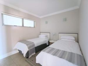 two beds in a white room with a window at The Aqua - Sleeps 4 - Patio & Sea Views in Plettenberg Bay