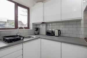 a kitchen with white cabinets and a sink and a window at Lovely House in Dagenham / Barking with free parking, WiFi & Garden in Dagenham