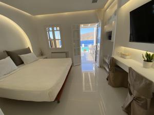 a white bedroom with a bed and a television at SeaRock Rooms and Suites in Amorgos