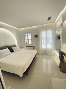 a white bedroom with a large bed and windows at SeaRock Rooms and Suites in Amorgos