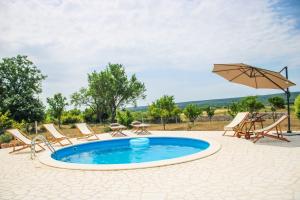 un patio con piscina, sillas y sombrilla en Villa Stone Pearl with heated swimming pool, en Sveti Filip i Jakov