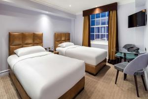 a hotel room with two beds and a desk at Radisson Blu Edwardian Bond Street Hotel, London in London