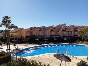 a swimming pool with umbrellas in front of some houses at Adosado playa Islantilla campo de golf in Huelva