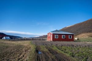 una casa roja en un campo con montañas al fondo en Sandhaugar Guesthouse, en Kiðagil