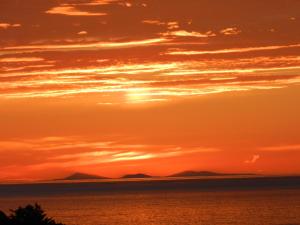 an orange sunset over the ocean with mountains in the background at Borve House, Kilchoan in Kilchoan