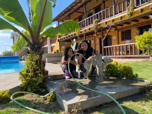 two girls sitting next to a fountain in front of a house at Hostería Colibri Aeropuerto in Tababela