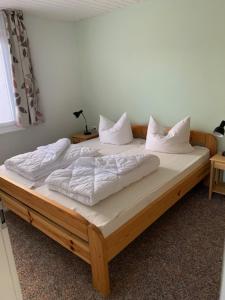 una cama de madera con sábanas blancas y almohadas. en Feriendorf Boeker Mühle, en Boek