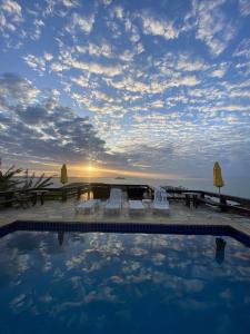 a swimming pool with chairs and a table and the ocean at Pousada Mirante dos Papagaios in Búzios