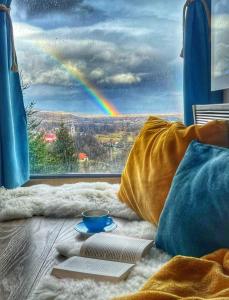 um arco-íris visto através de uma janela com um livro e uma chávena de café em Tiny House Retreat Bran em Bran