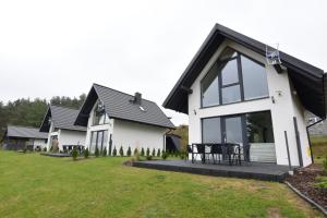 a white house with a black roof at Domki U Zbyszka nad jeziorem z balią ogrodową! in Kiedrowice