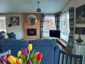 una sala de estar con un sofá azul y flores en Sycamore Lodge Auchterarder en Auchterarder