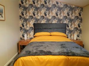 um quarto com uma cama com lençóis amarelos e um papel de parede em Sycamore Lodge Auchterarder em Auchterarder