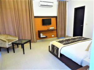 um quarto com uma cama, uma cadeira e uma televisão em Tavisha Villa Flim City Road Dadri Road em Noida