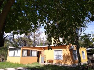 Una casa amarilla con un árbol delante. en Cuatro Estaciones en General Rodríguez
