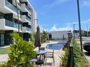 ein Tisch mit Stühlen und einem Sonnenschirm neben einem Gebäude in der Unterkunft Flat ESTUDIO de LUXO - Praia de Muro Alto - Piscinas - Ideal para CASAIS, famílias com crianças - ap COMPLETO - AR COND, WI FI, NETFLIX, ESTACIONAMENTO - 400 mt do MAR in Porto De Galinhas