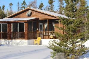 a log cabin with a porch in the snow at 1 and Only Riverside Accommodations in Sable River