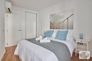 a white bedroom with a large bed with blue pillows at Dulce Arbolí Little Apartments in Cádiz