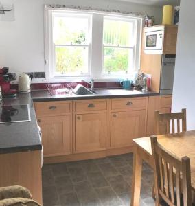 a kitchen with wooden cabinets and a sink and two windows at Abbey Green, New Abbey, Dumfries and Galloway in Dumfries