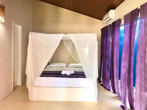 a bed with a canopy in a room with purple curtains at Casa Colorida in Pipa