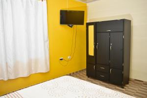 Hotel Tari في Mocoa: غرفة نوم مع خزانة سوداء وتلفزيون على جدار أصفر